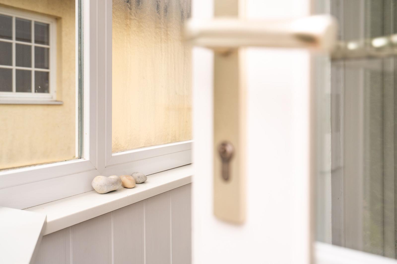 Draußen vor dem Fenster liegen drei Steine auf dem Sims. Die Tür ist leicht geöffnet.