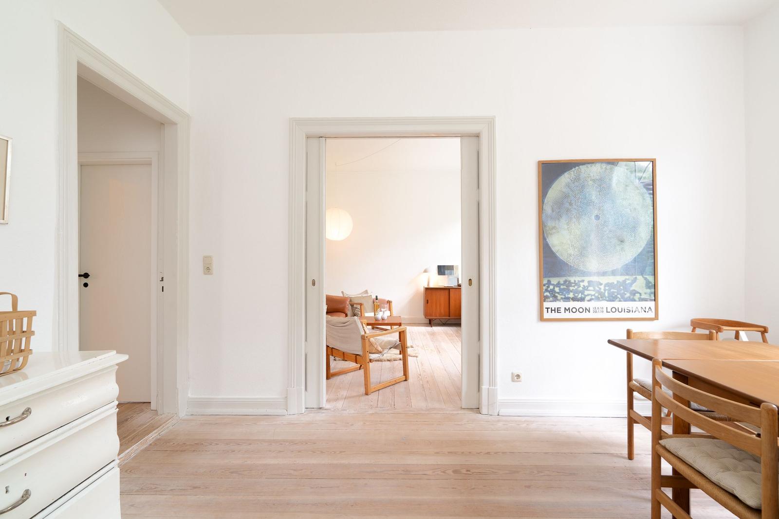 Helle Wohnung mit Essbereich und Blick in Wohnzimmer. Wandbild und Holzmöbel.