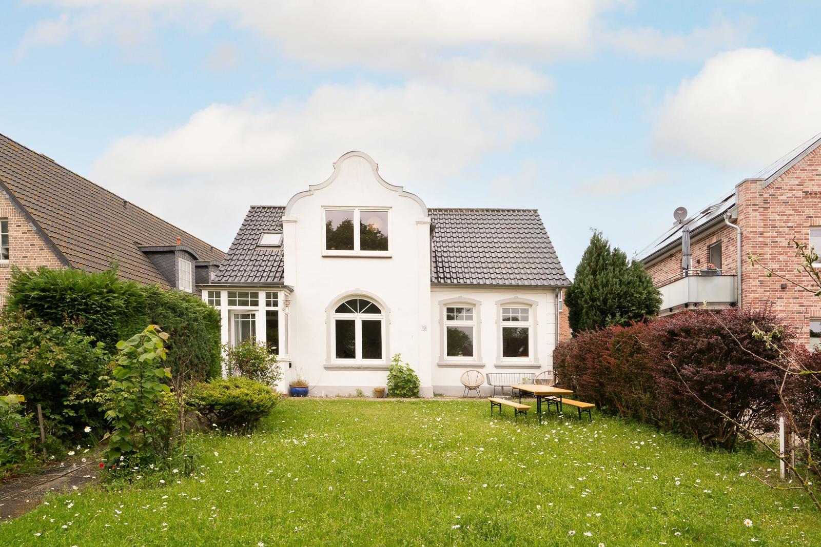 Weißes Haus mit Garten, Tisch und Bänken. Grasfläche mit Blumen.
