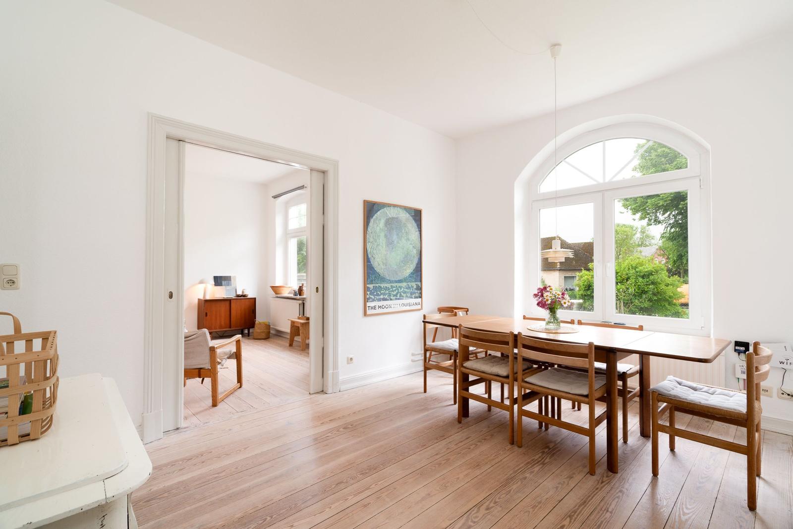 Esszimmer mit Holztisch, Stühlen und großem Fenster. Durchgang zu Wohnzimmer mit Möbeln.