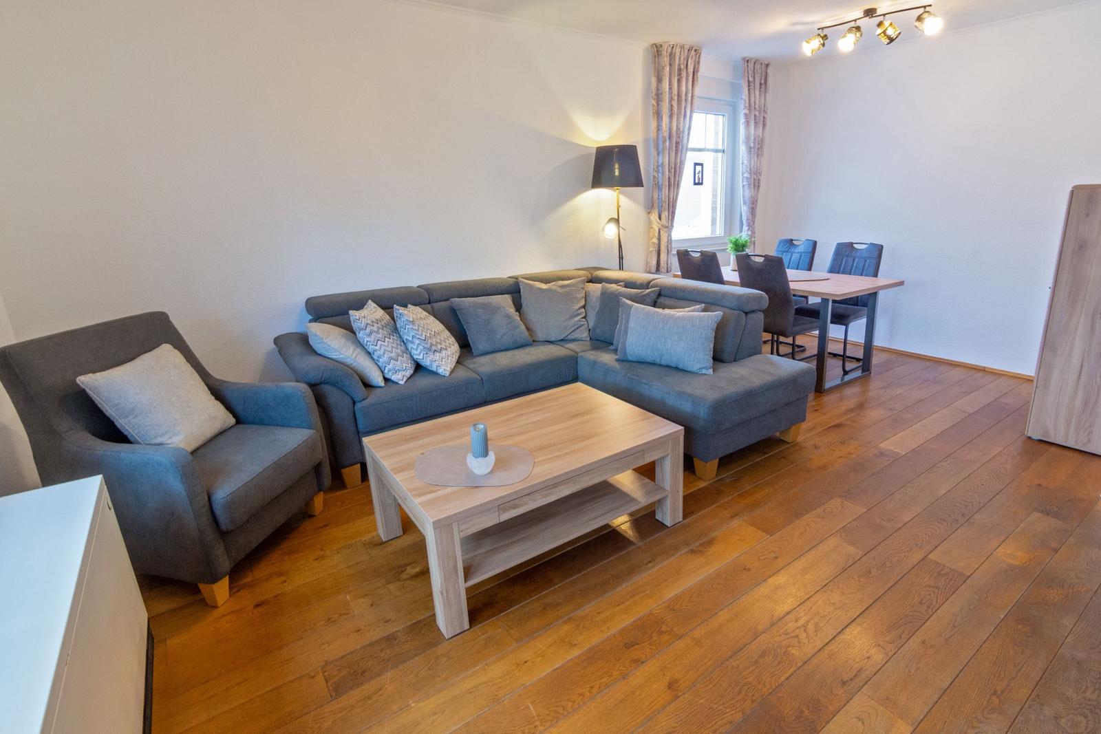 Wohn- und Essbereich mit Sofa, Sessel, Tisch und Stühlen auf Holzboden.