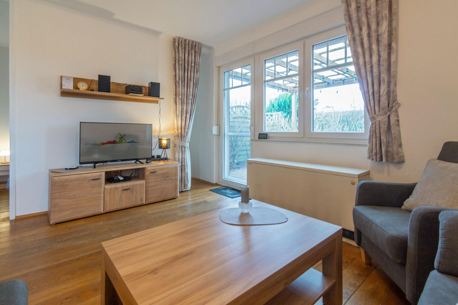Wohnzimmer mit Holztisch, Sofa, Fernseher und Fenster zum Garten.