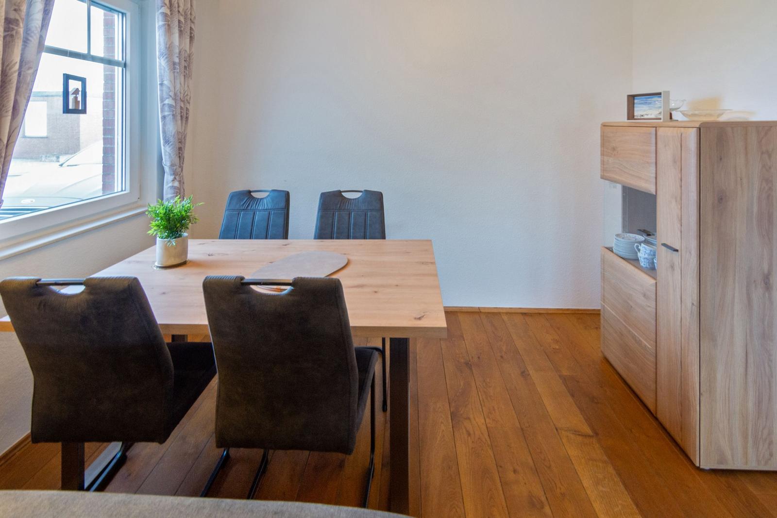 Esszimmer mit Holztisch, vier Stühlen und Holzboden. An der Wand steht ein Schrank.