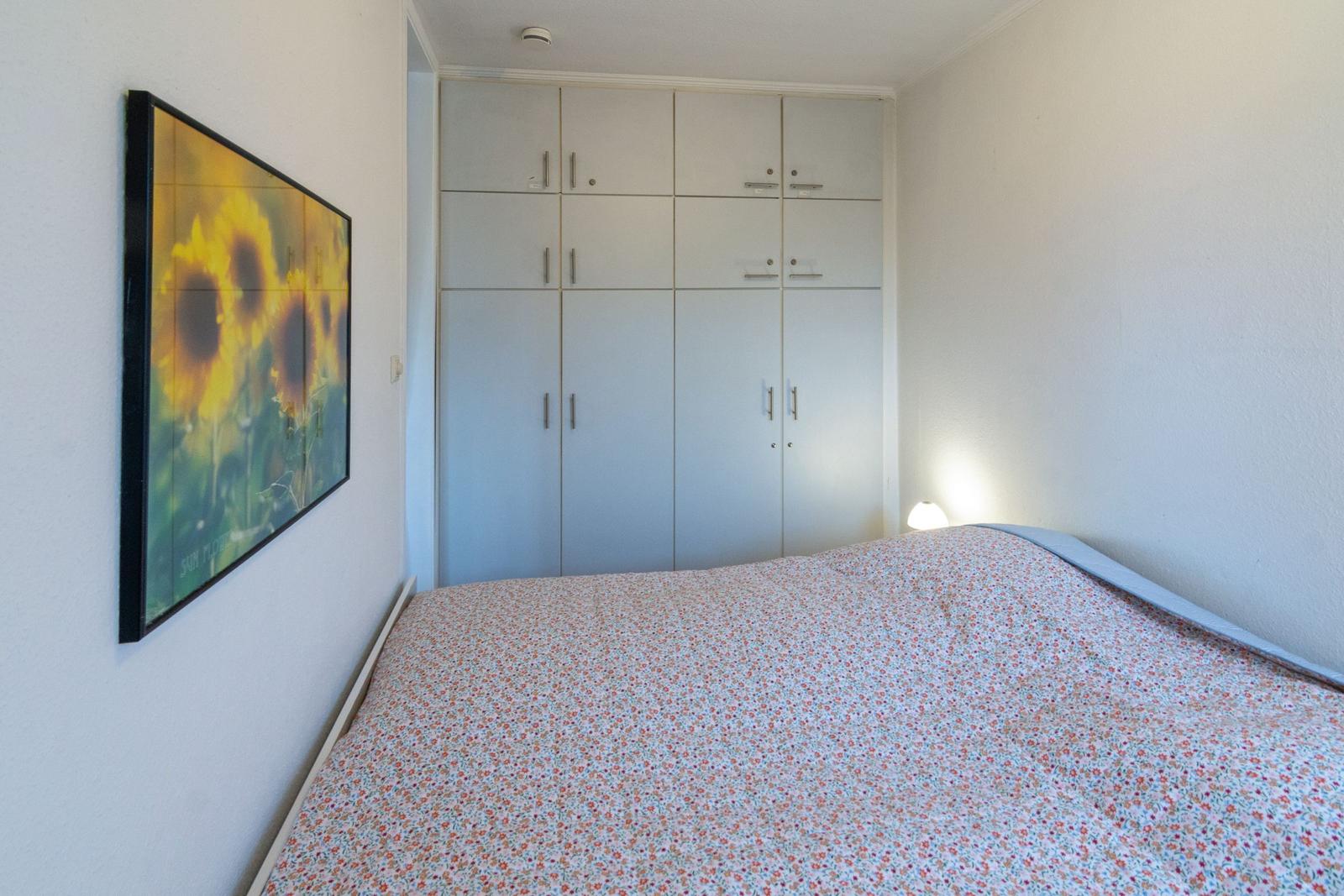 Schlafzimmer mit Bett, Kleiderschrank und Wandbild mit Sonnenblumen.