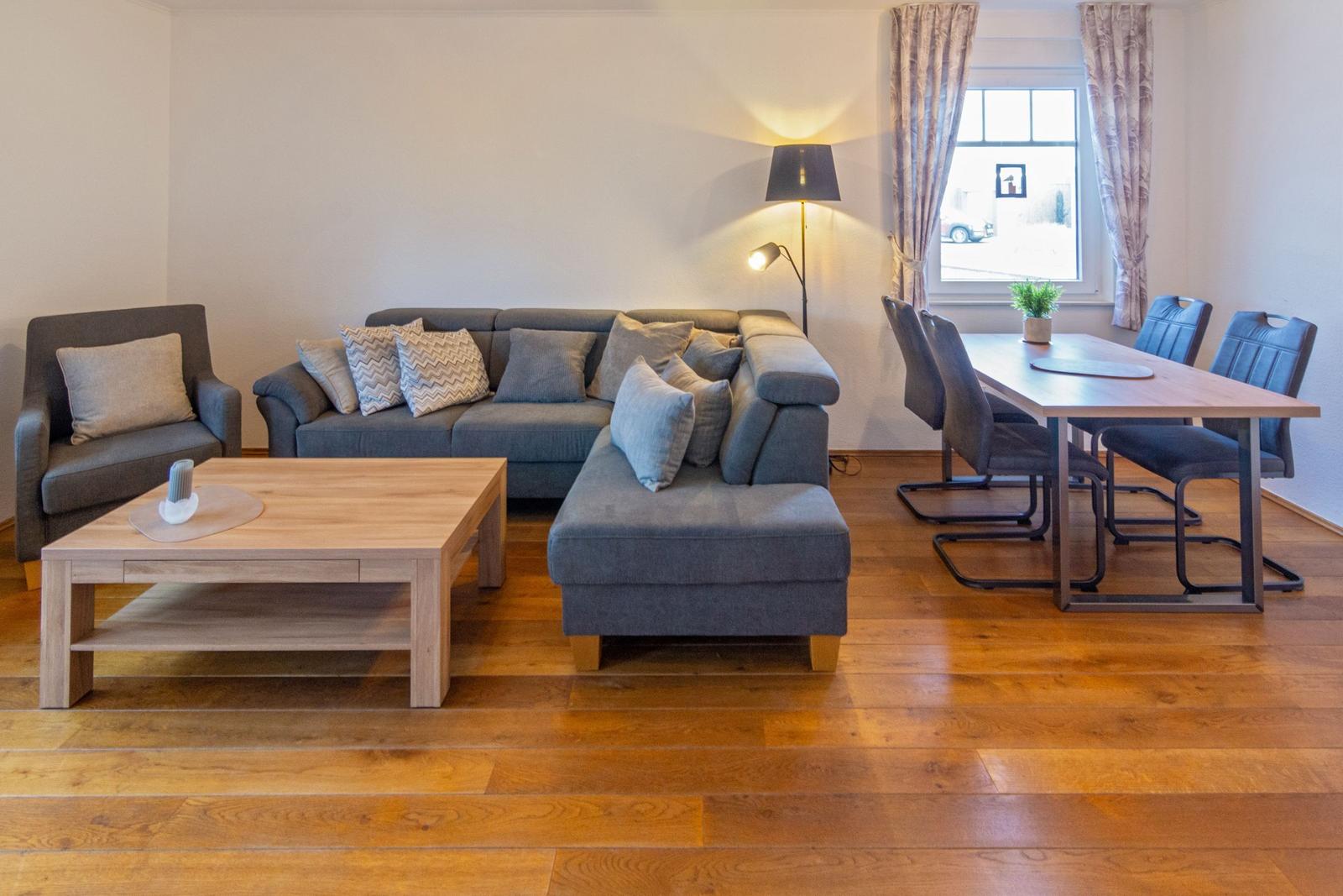Wohn- und Essbereich mit Sofa, Sessel, Tisch und Stühlen auf Holzboden.