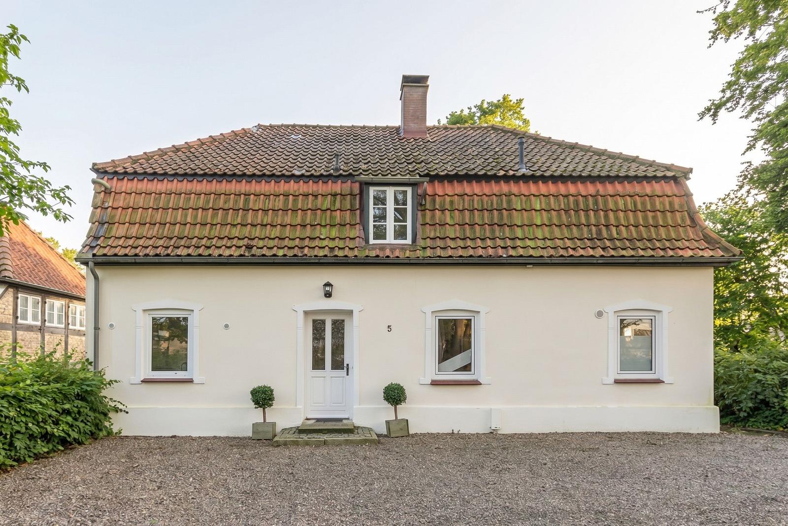 House with red tiled roof, white facade, and garden with plants.