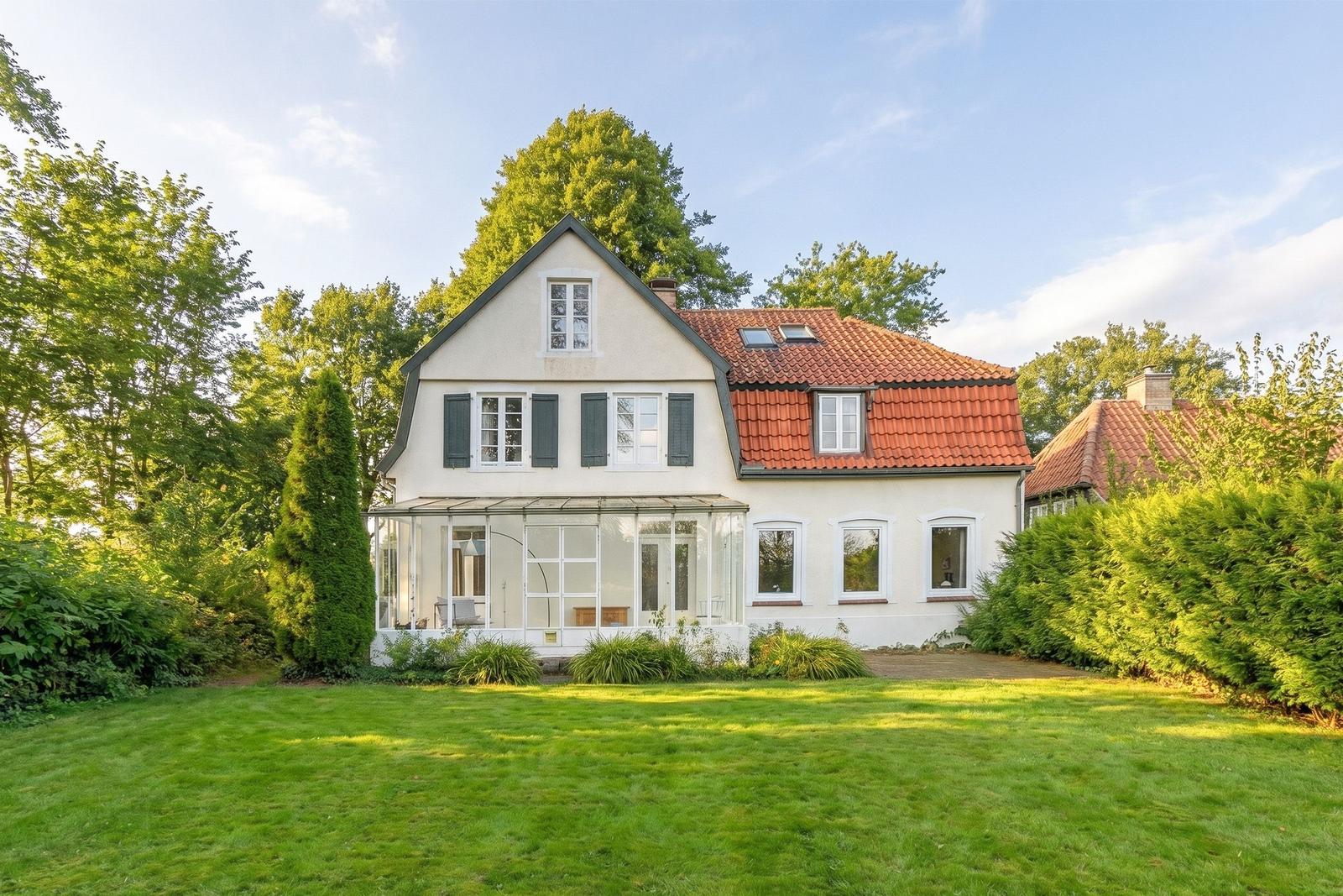 House with red roof and green garden. Glass veranda and windows visible.