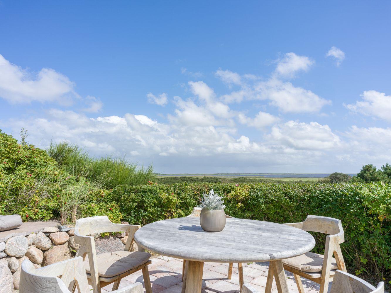 Runder Tisch mit Stühlen auf Terrasse mit Blick auf Grünflächen und Himmel.