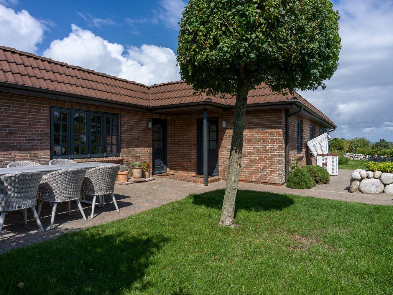 Haus mit Terrasse, Tisch, Stühlen und Baum im Vorgarten.