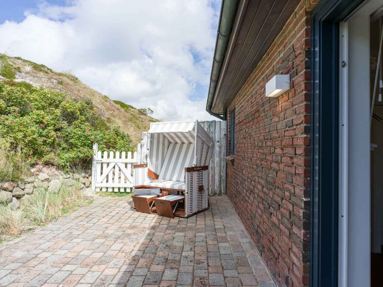 Terrasse mit Strandkorb, rotem Backsteinhaus und grüner Hang