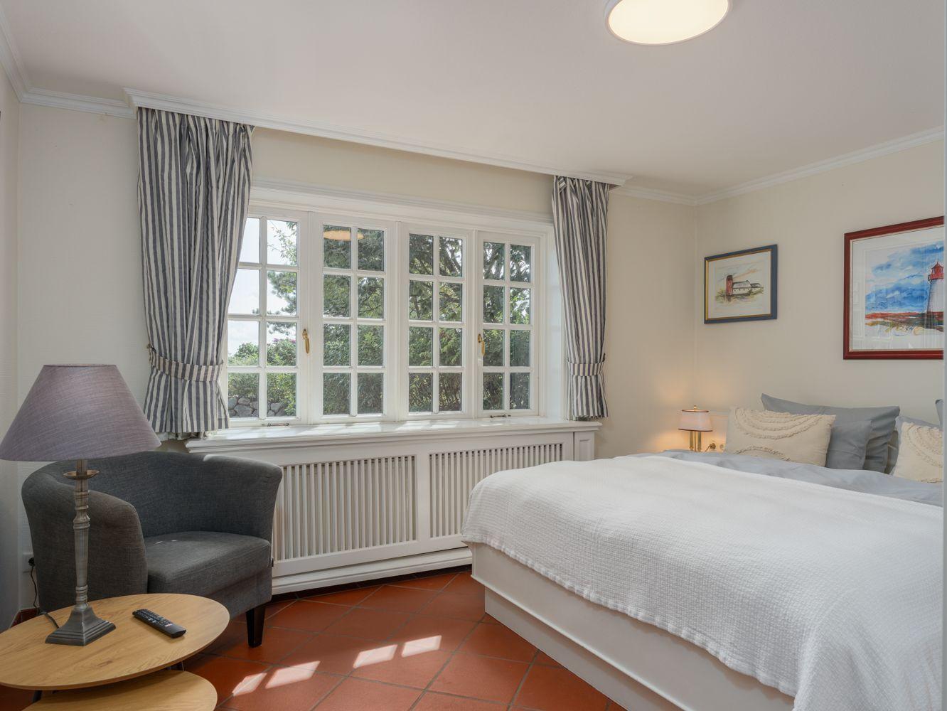 Schlafzimmer mit Bett, Sessel und Fenster mit Blick auf Grün.