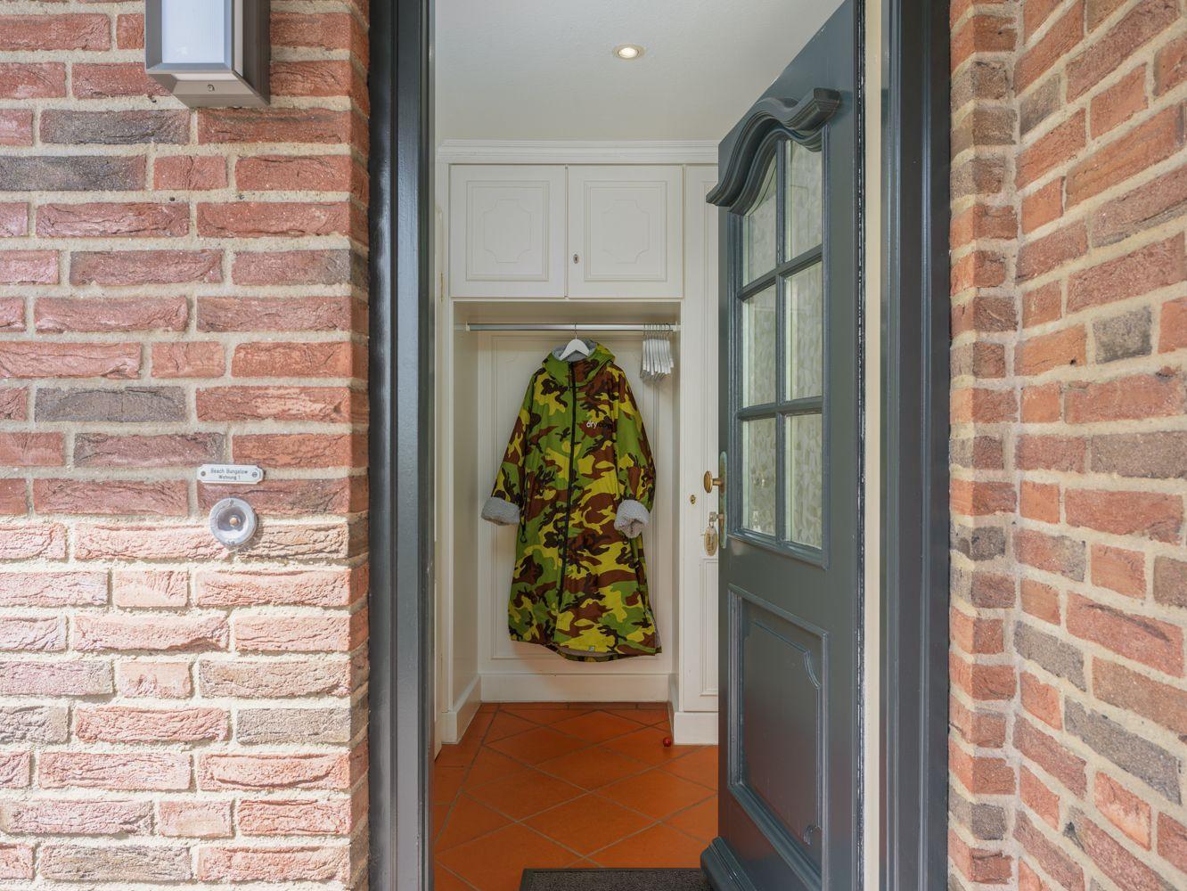 Eingangsbereich mit Kleiderständer und Regal, ein Camouflage-Mantel hängt daran.
