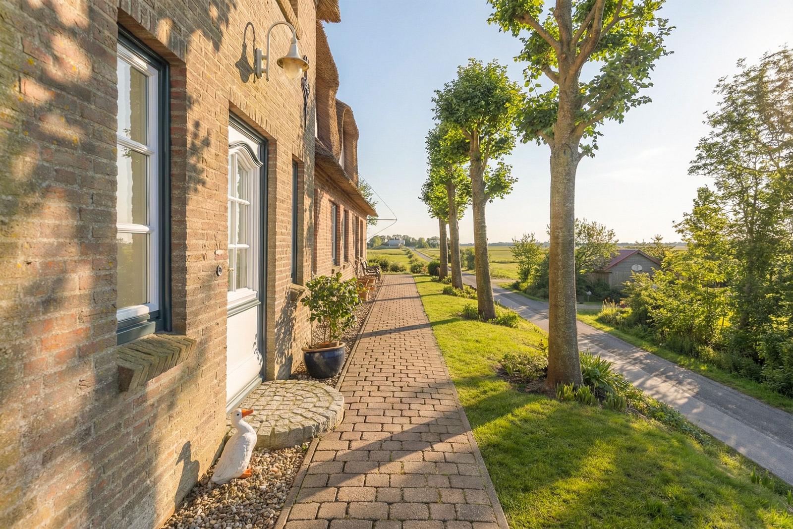Haus mit Steinweg, Bäumen und grünem Rasen. Weiße Ente vor der Tür.