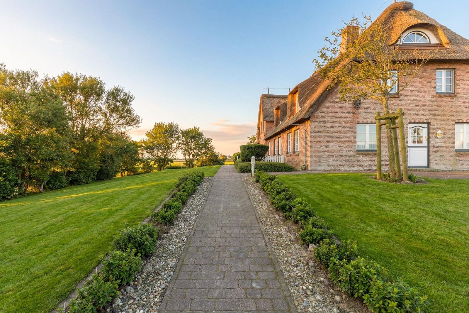 Haus mit Strohdach und gepflastertem Weg durch grünen Garten.