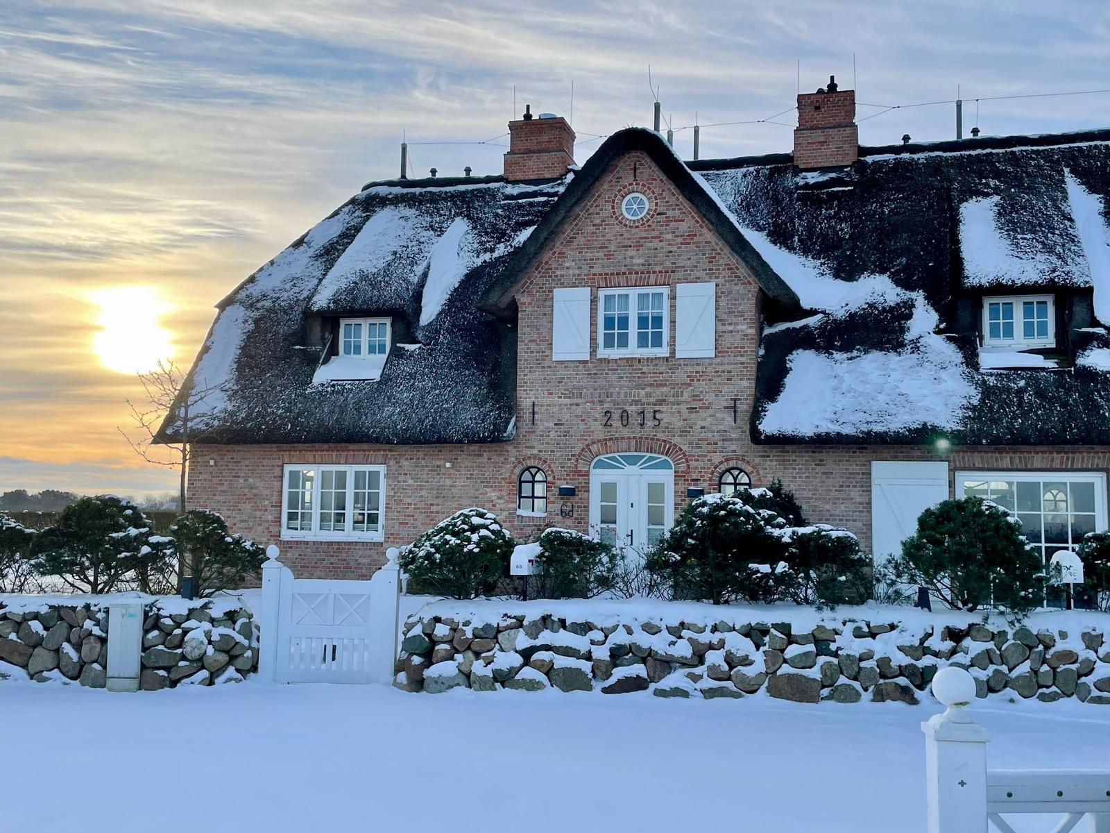 Schneelandschaft vor einem traditionellen Haus mit Strohdach und Backsteinfassade.