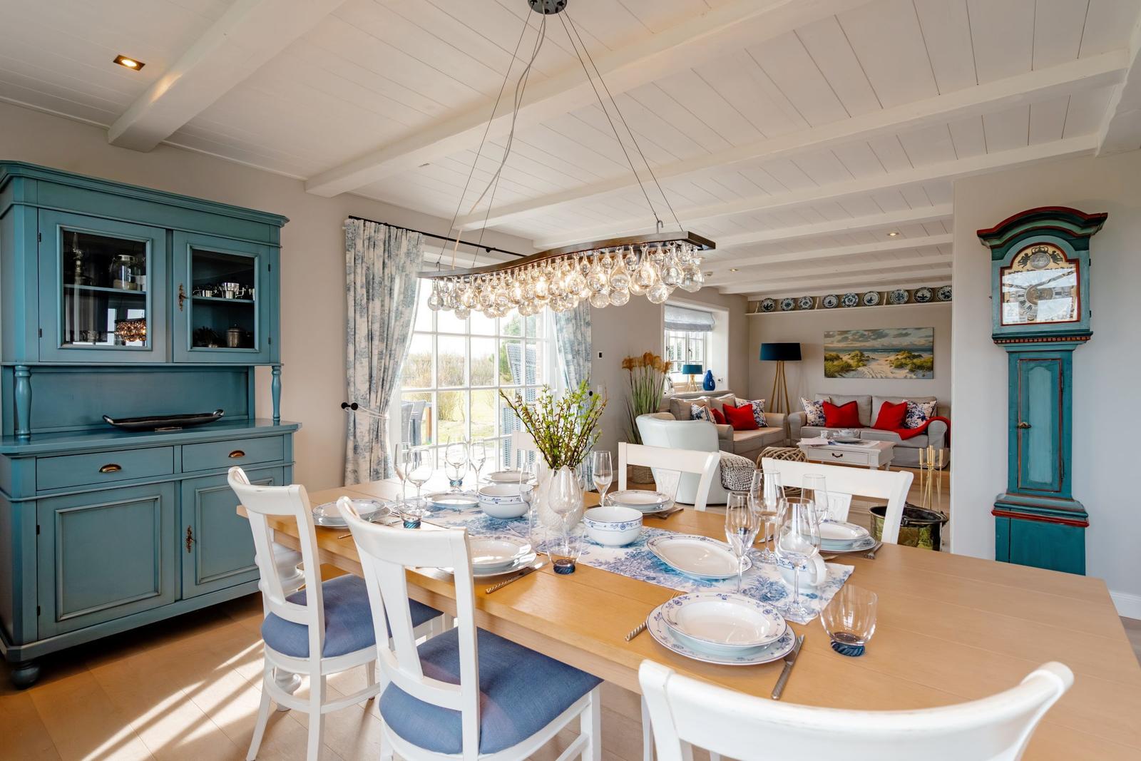 Esszimmer mit Tisch, Stühlen und blauem Sideboard. Im Hintergrund Wohnbereich mit Sofa und Stehlampe.