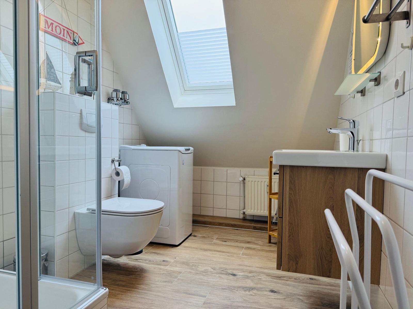 Badezimmer mit Dusche, WC, Waschmaschine und Dachfenster.