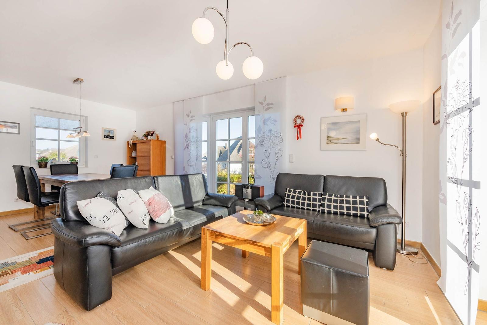 Wohn- und Essbereich mit zwei schwarzen Sofas, Holztisch und Fenster zur Aussicht.