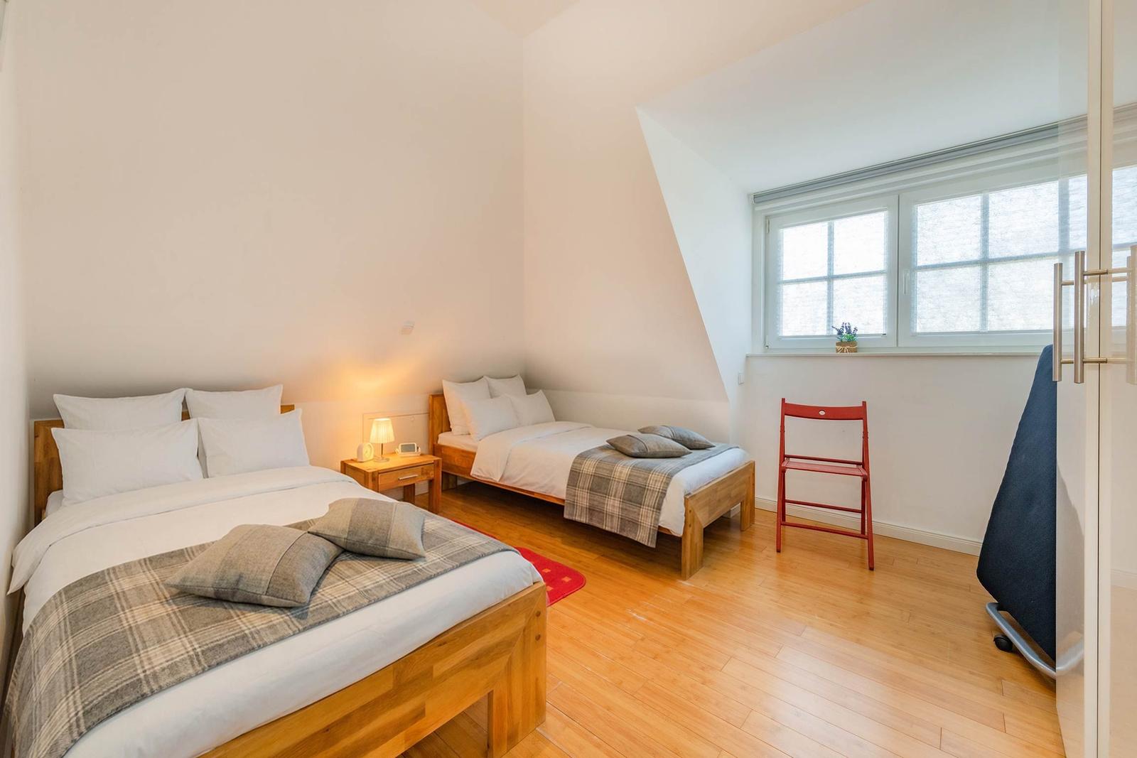 Zimmer mit zwei Betten, Holzboden und Fenster. Ein roter Stuhl steht daneben.