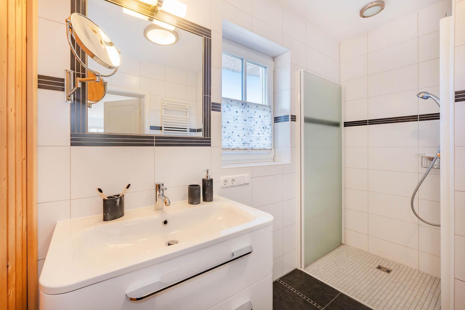 Badezimmer mit Dusche, Waschbecken und Spiegel. Fenster mit Vorhang.