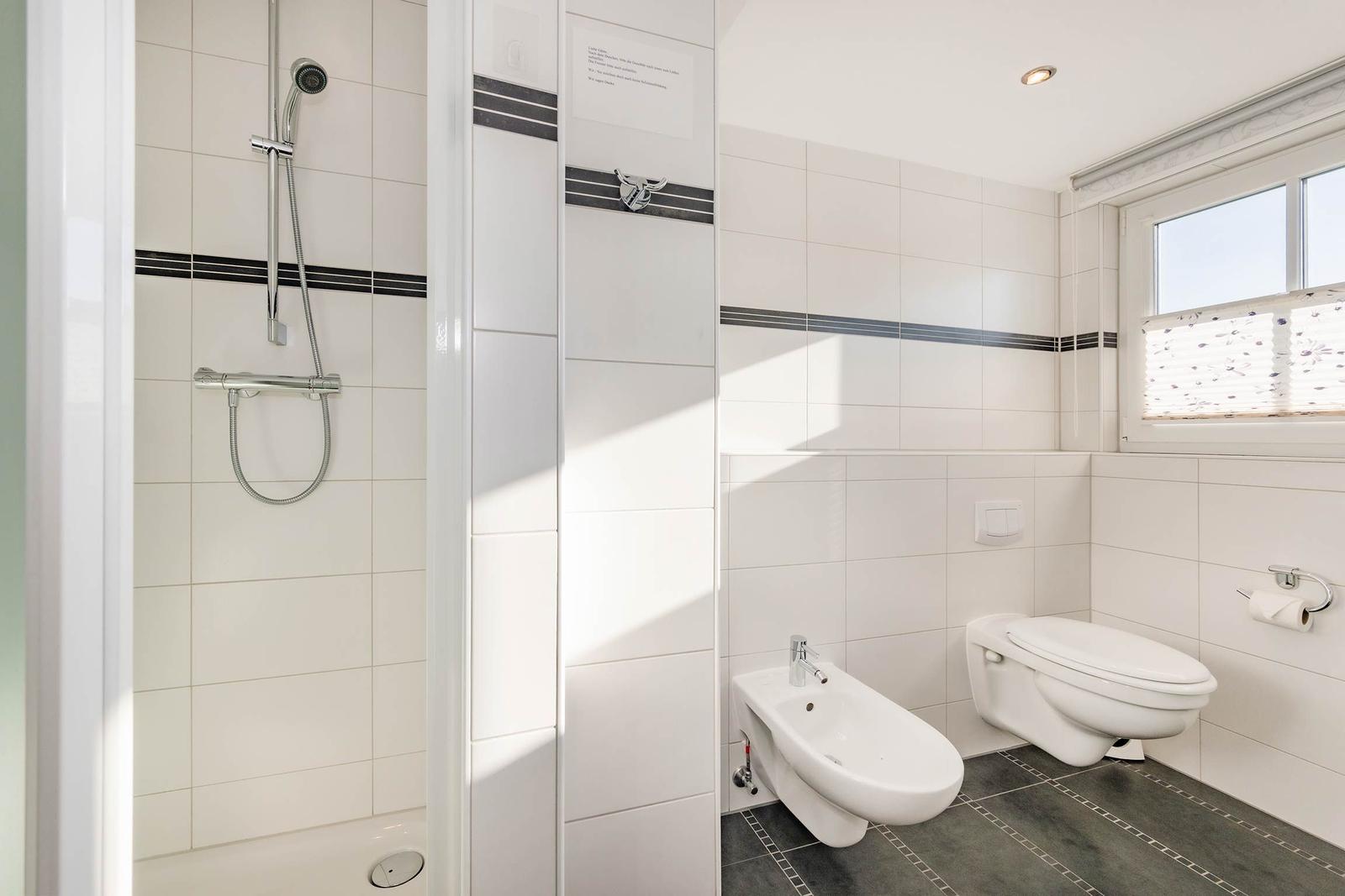 Badezimmer mit Dusche, WC und Bidet. Weiße Fliesen mit dunklen Streifen.