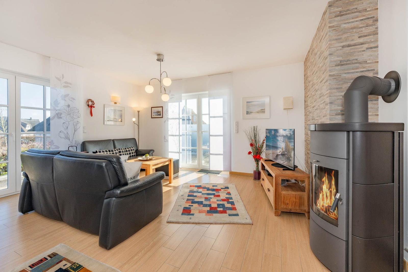 Wohnzimmer mit Sofa, Kamin und TV. Holzboden und große Fenster.