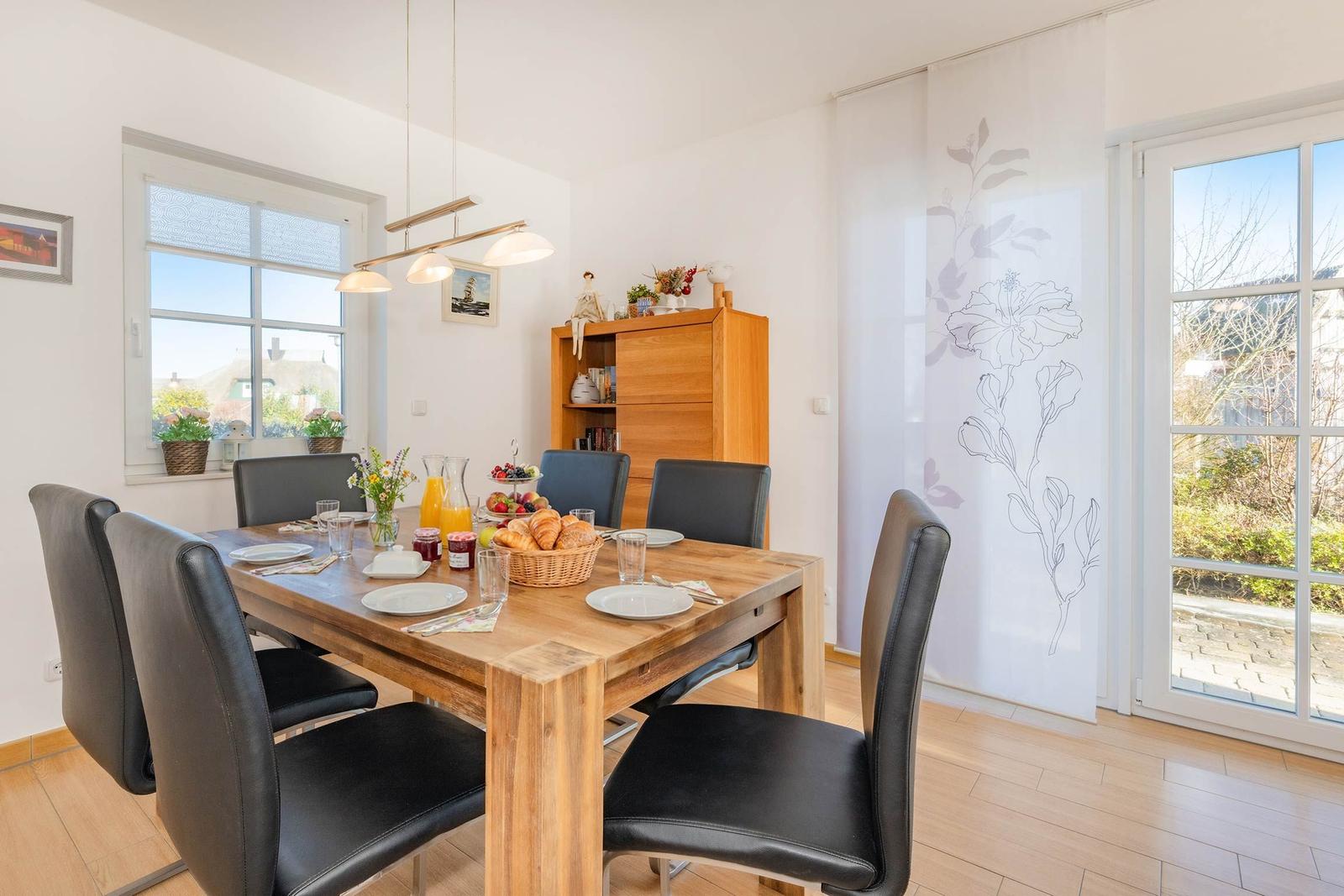 Esszimmer mit Holztisch, schwarzen Stühlen und Fensterblick auf Garten.