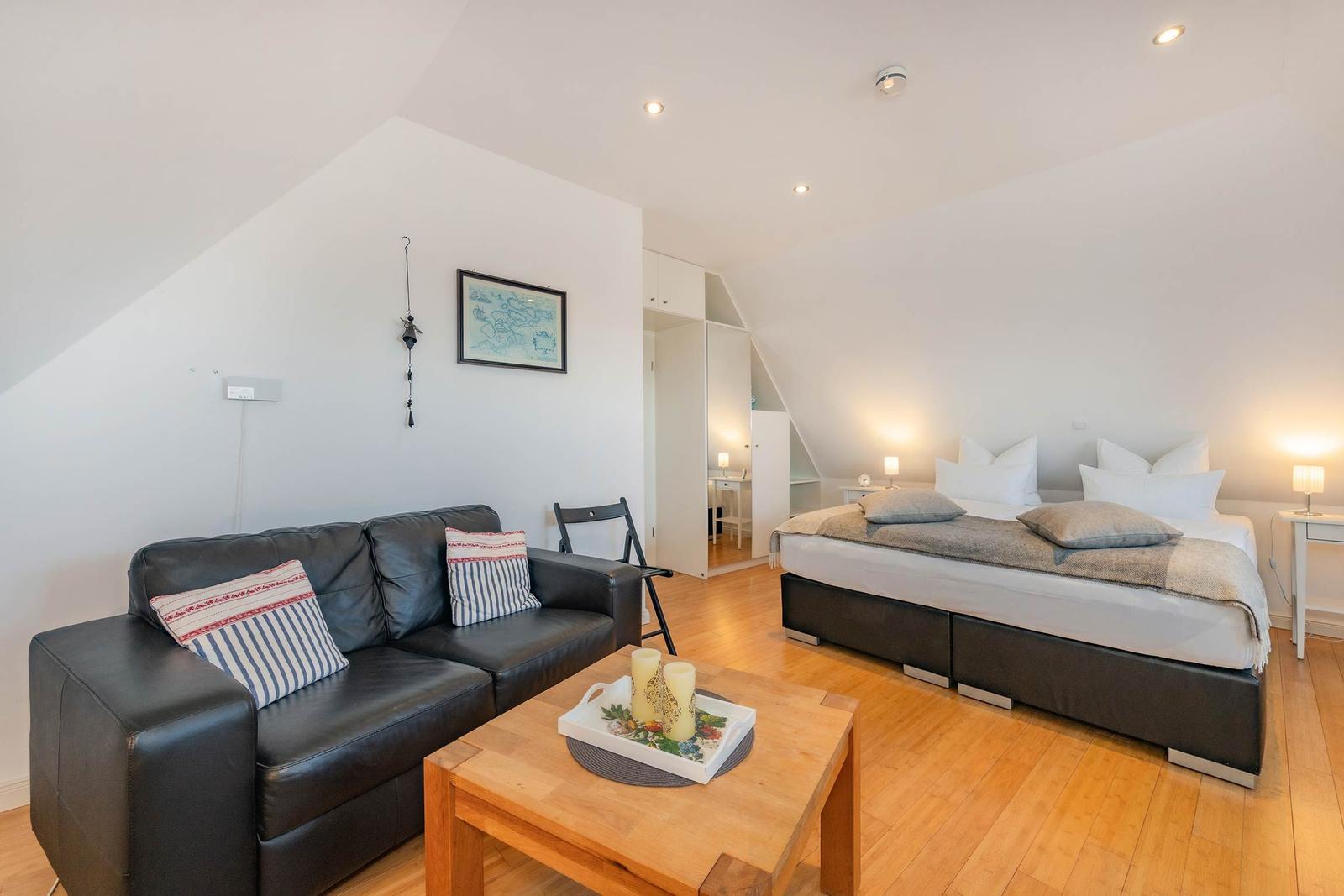 Schlafzimmer mit Sofa, Bett und Holzboden. An der Wand hängt ein Bild.
