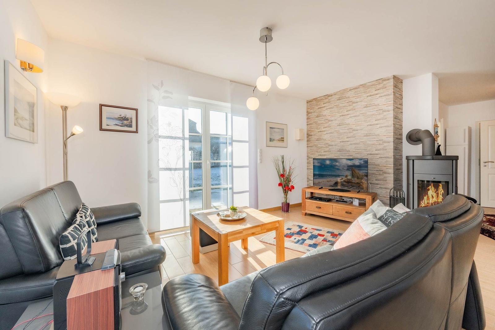 Wohnzimmer mit Sofa, Fernseher und Kamin. Türen führen auf eine Terrasse.