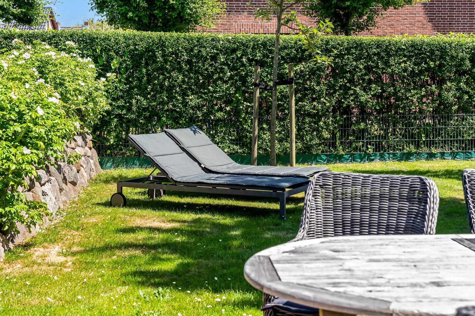 Garden with sun loungers, table and chairs. Backyard with hedge and stone wall.