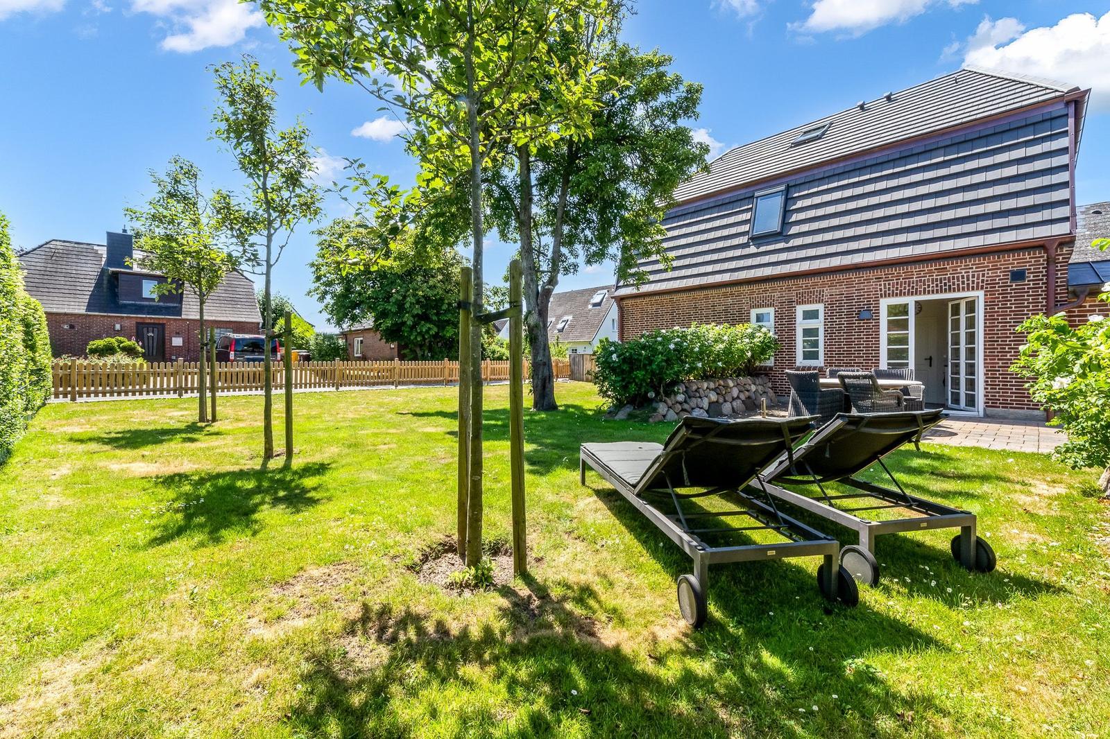 House with garden, sun loungers, and terrace. Lawn and trees visible.