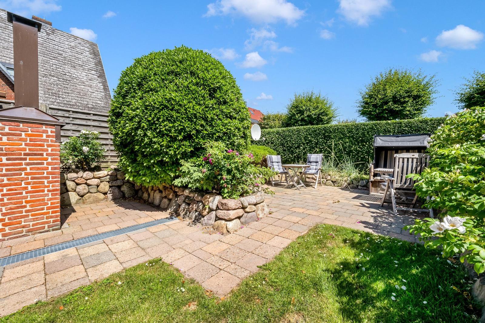 Garden with paving, green areas, seating, and stone wall.