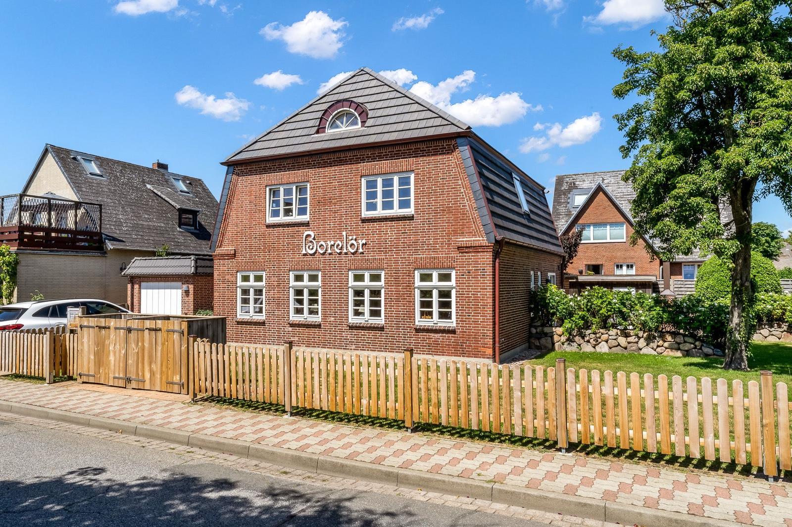 Red brick building with wooden fence and green lawn under a blue sky.