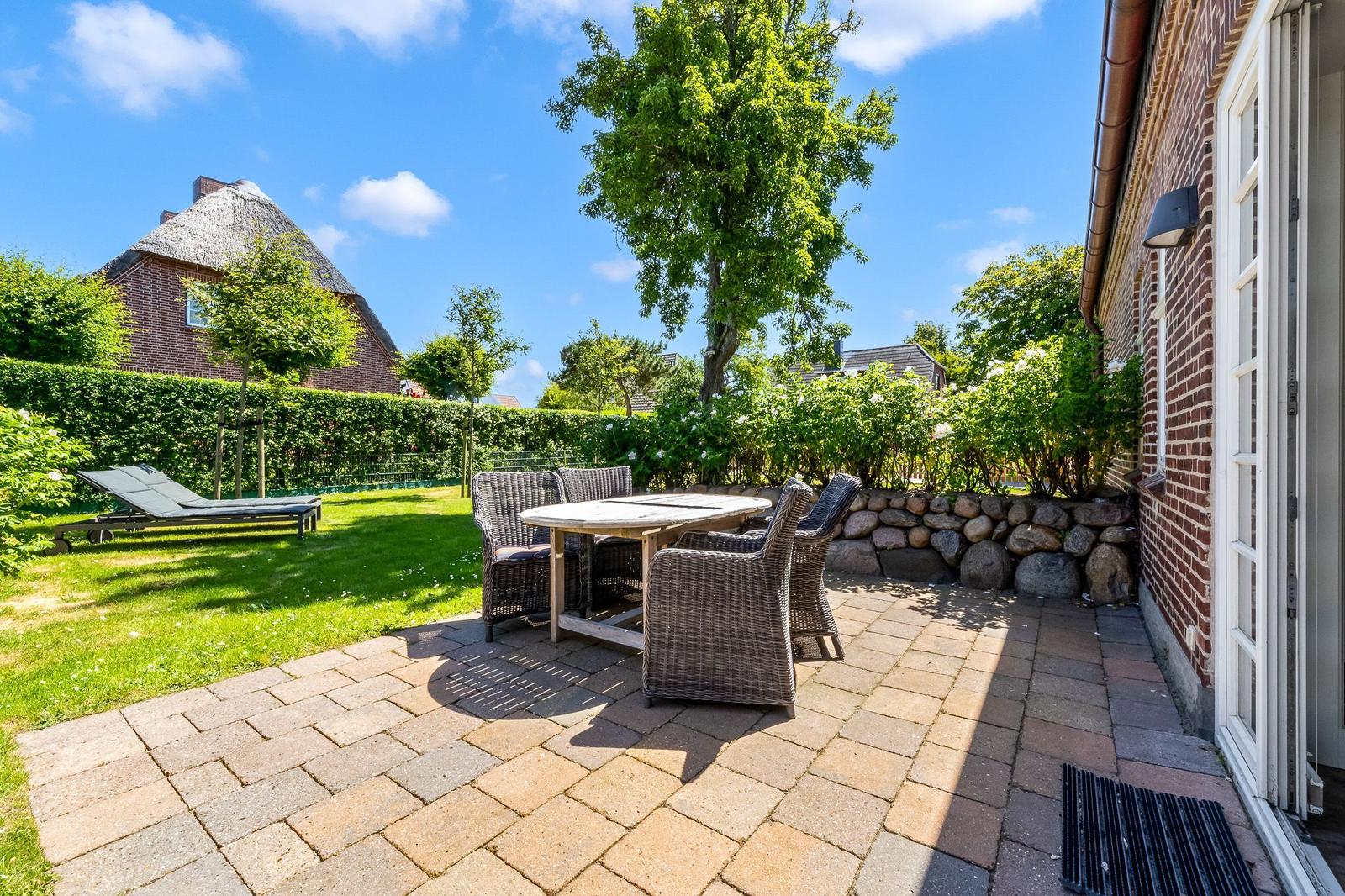 Terrace with table and chairs, garden area with lounge chair and greenery.