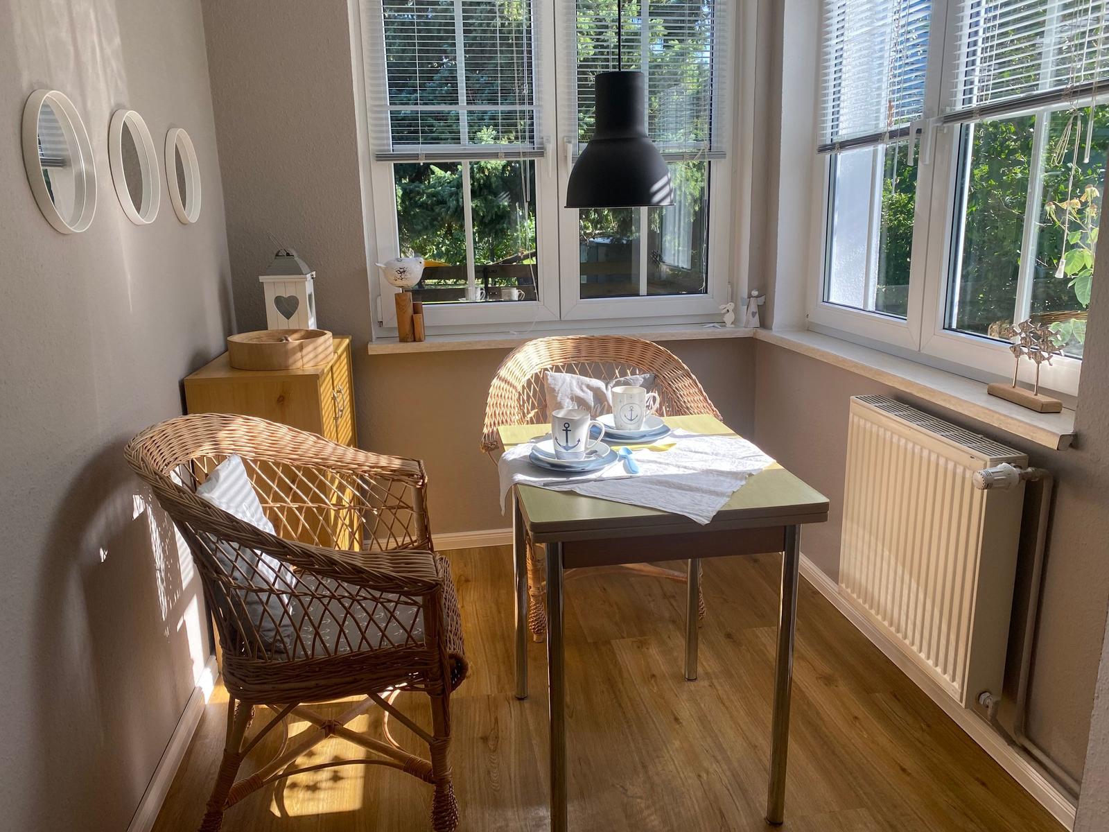 Dining table with two chairs, windows with blinds and wooden floor.