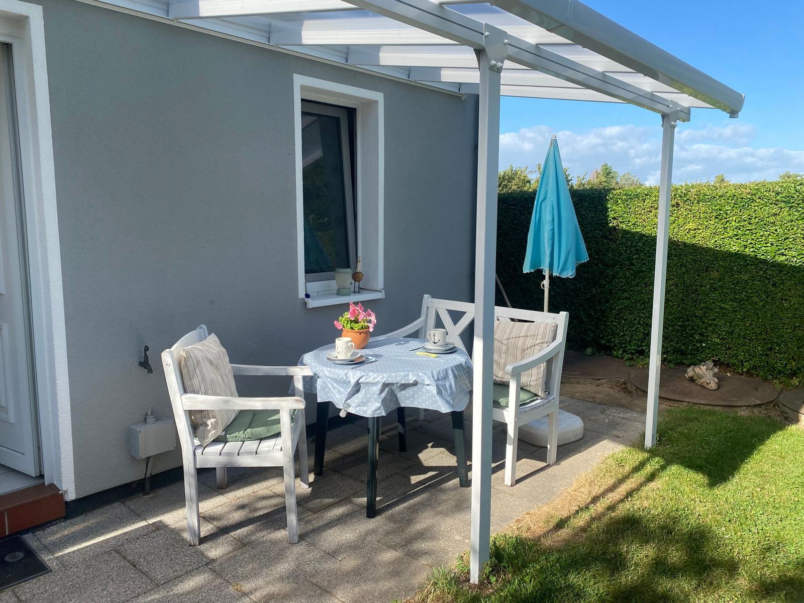 Terrace with table, two chairs, and blue umbrella under a white canopy.
