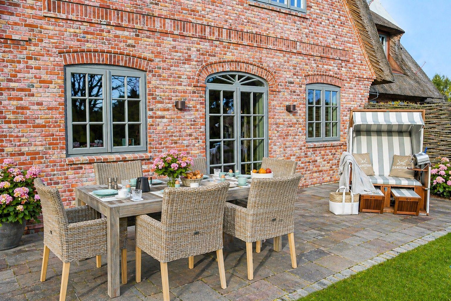 Terrasse mit Esstisch, Stühlen und Sonnenschutz vor Backsteinhaus