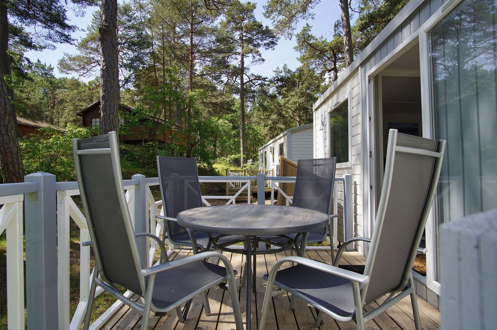 Terrasse mit Tisch und vier Stühlen vor einem Haus im Wald.