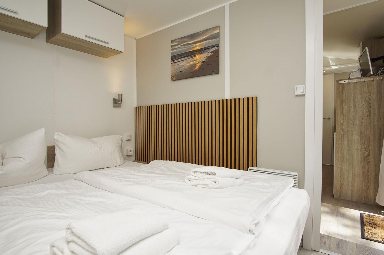 Schlafzimmer mit Doppelbett, Holz-Kopfteil und Wandbild.