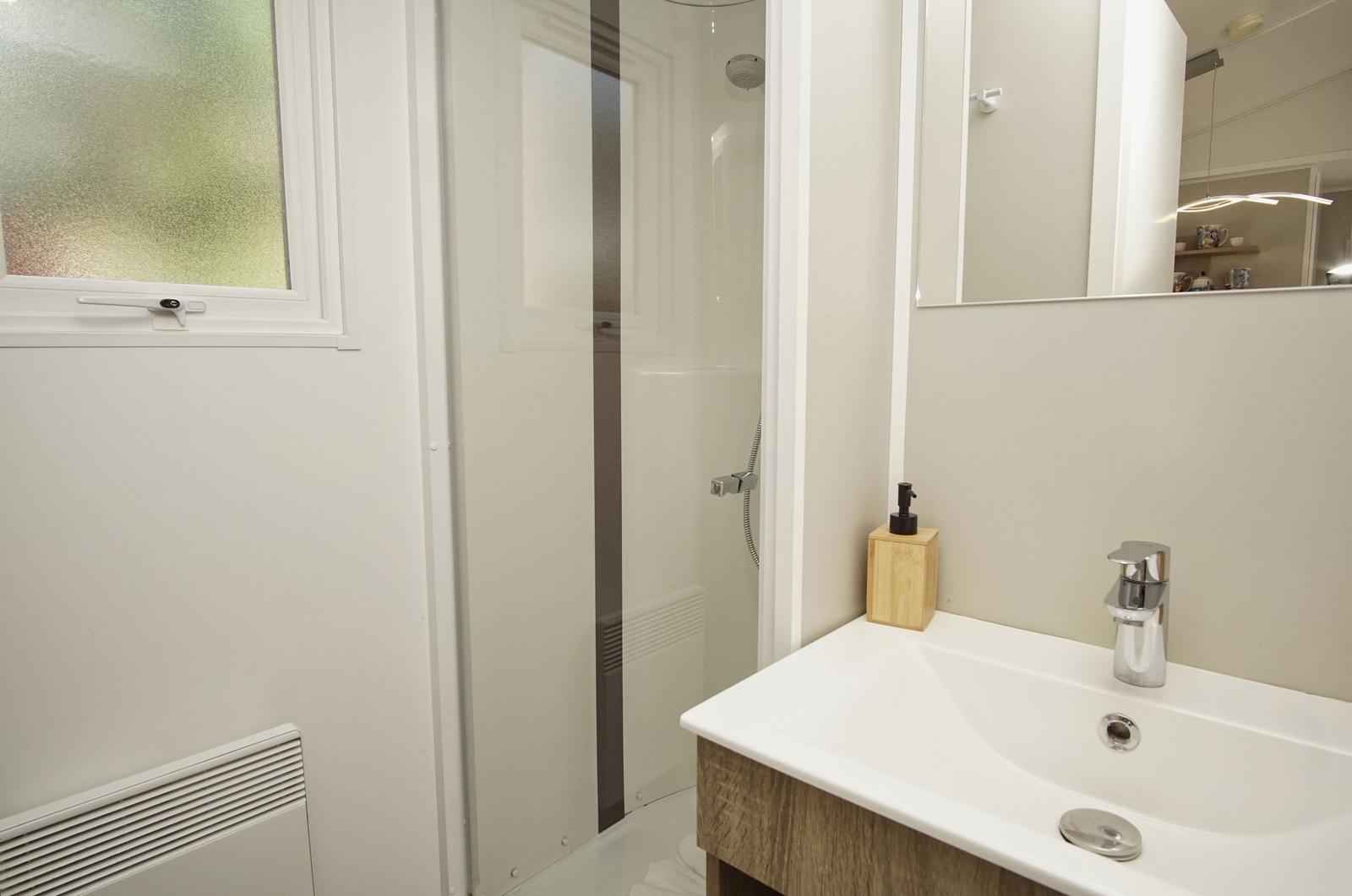 Badezimmer mit Dusche, Waschbecken und Spiegel. Fenster mit beschichtetem Glas.
