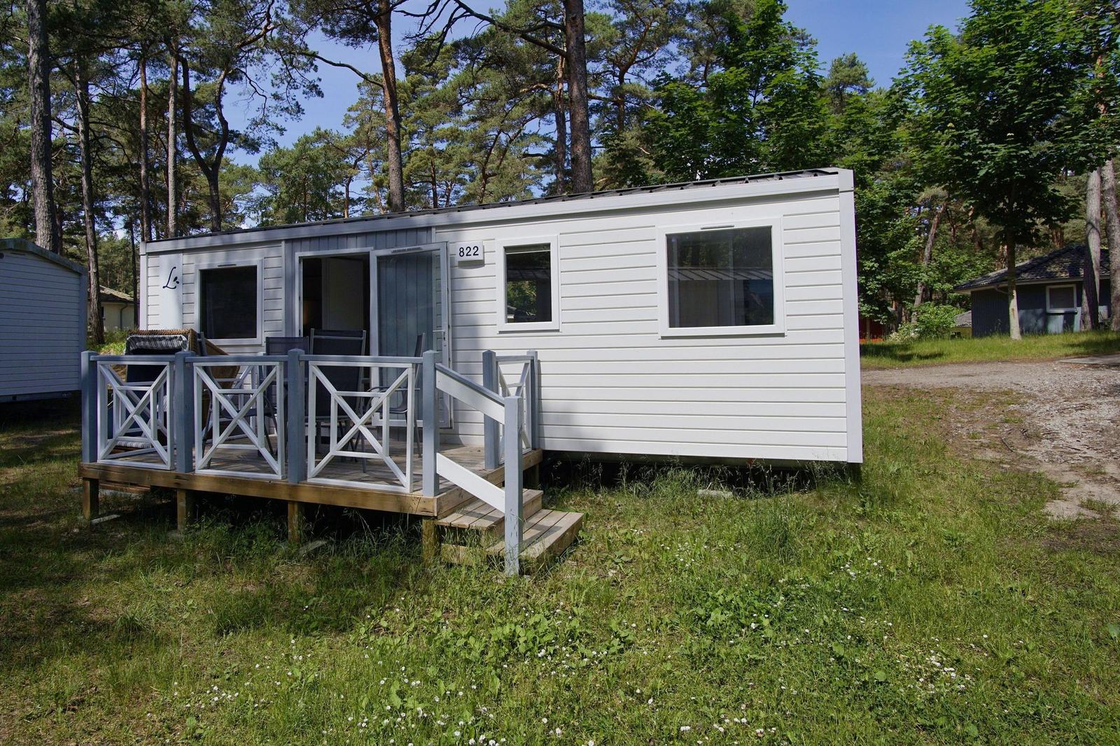 Weiße Ferienhütte mit Terrasse und Garten. Umgeben von Bäumen. Hausnummer 822.