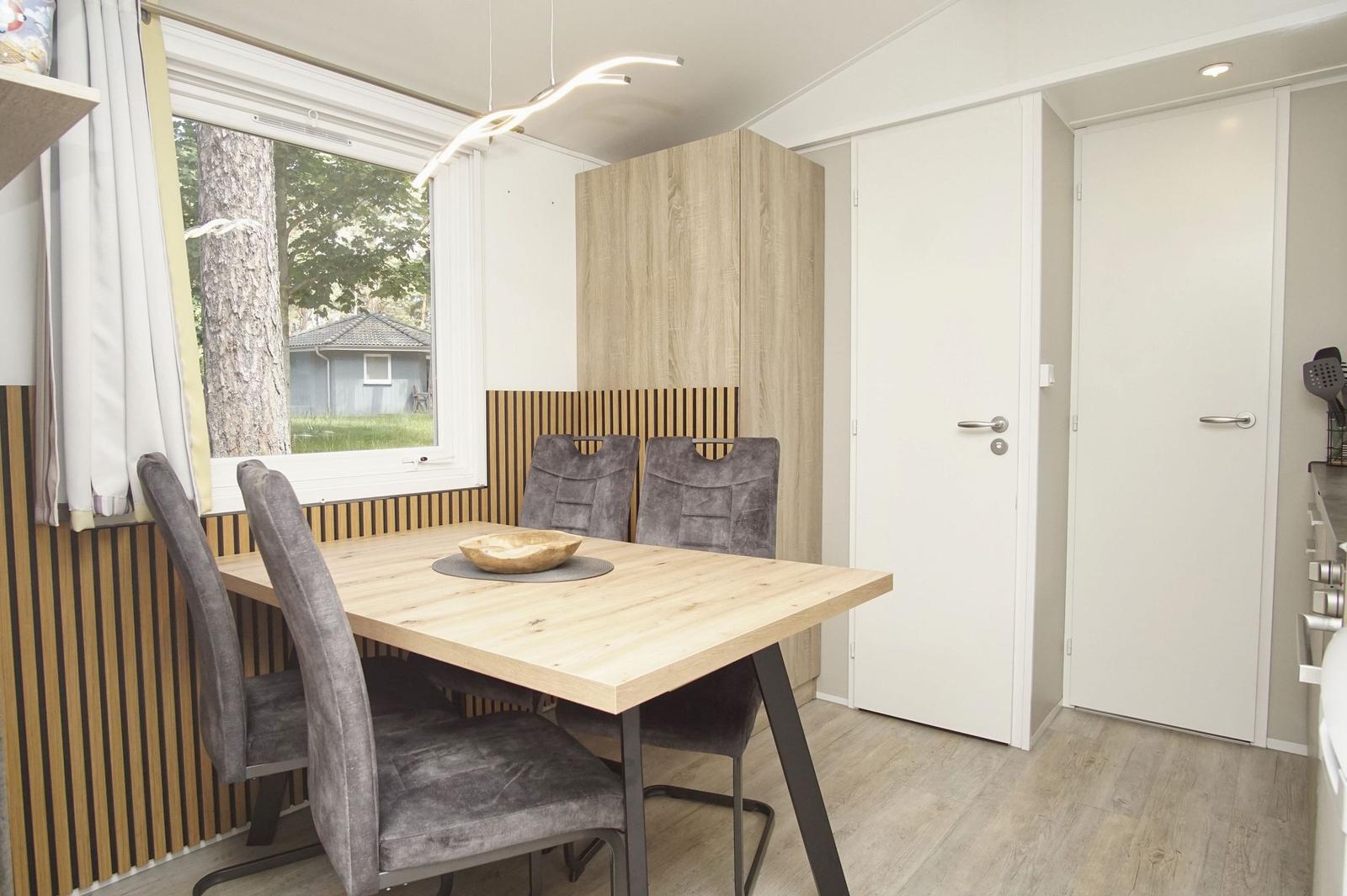 Essbereich mit Holztisch, vier Stühlen und Fensterblick auf Wald.