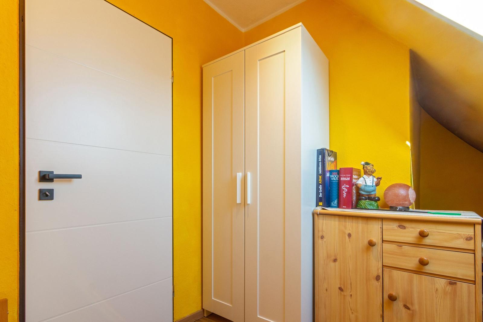 Schlafzimmer mit gelben Wänden, Schrank und Holzkommode.