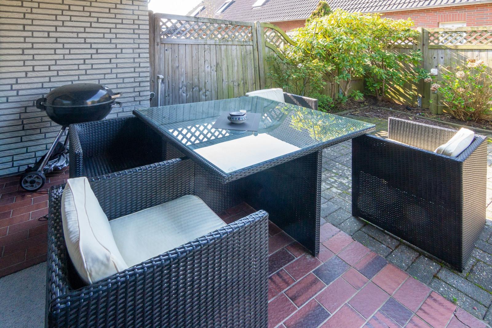 Außenbereich mit Gartentisch, vier Stühlen und Grill an Backsteinmauer.
