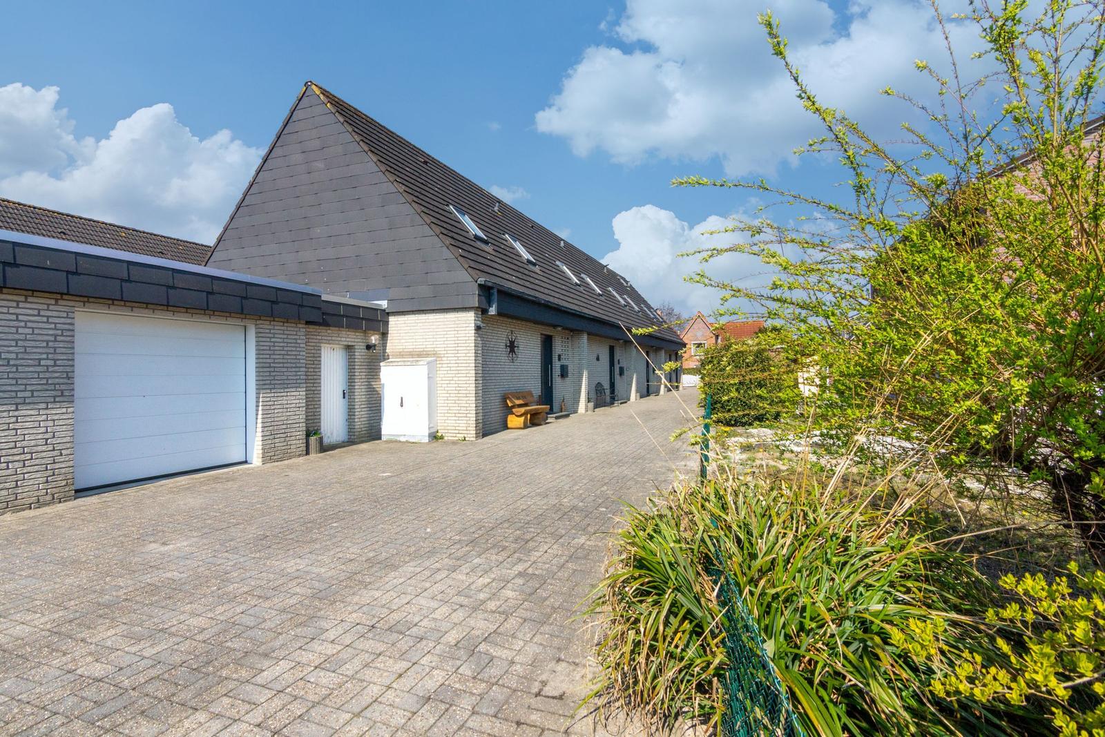 Moderne Villa mit Garage und gepflastertem Hof unter blauem Himmel.