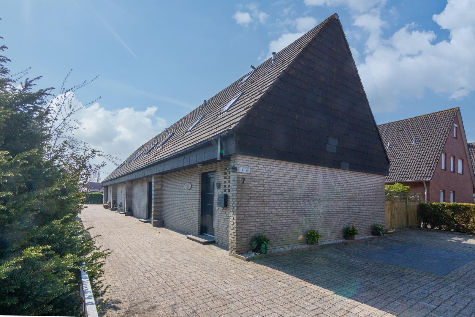 Moderne Villa mit Steinmauer und dunklem Dach, gepflastertem Hof und grüner Umgebung.