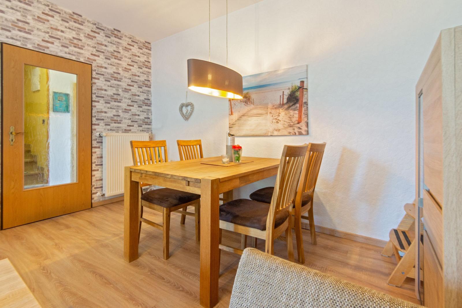 Essbereich mit Holztisch, vier Stühlen und Wandbild. Holzfußboden und Tür mit Glas.