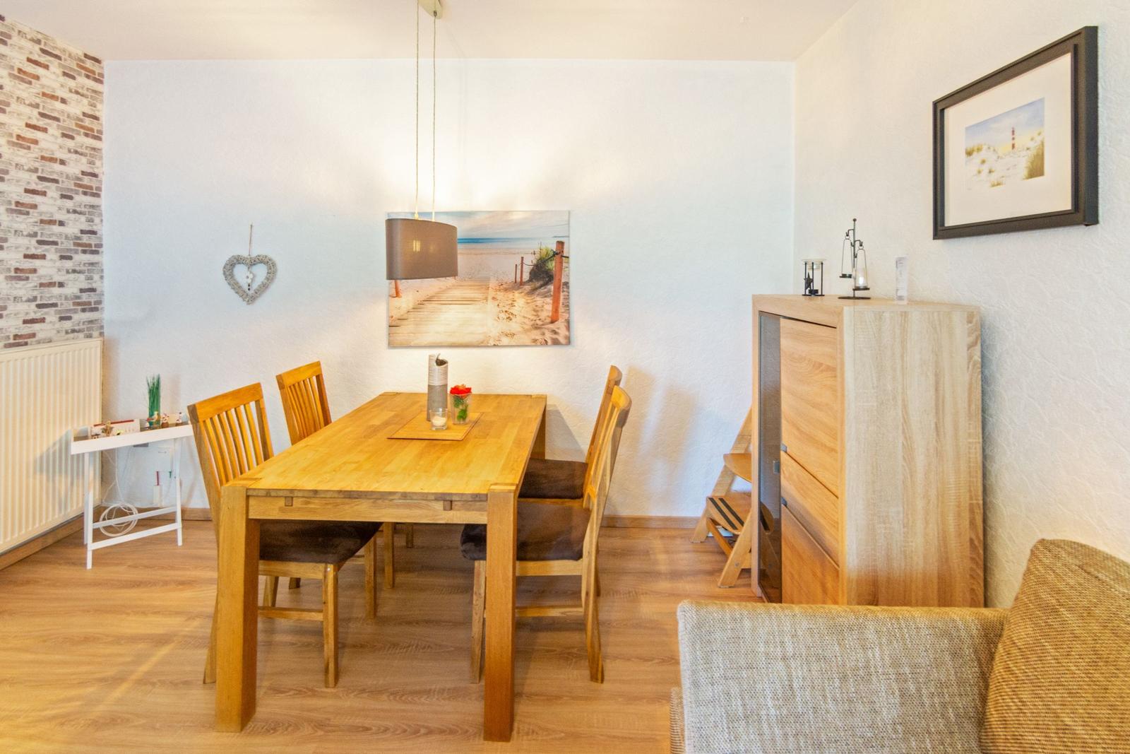 Essbereich mit Holztisch, Stühlen und Wandbild. Holzfußboden und Schrank sichtbar.