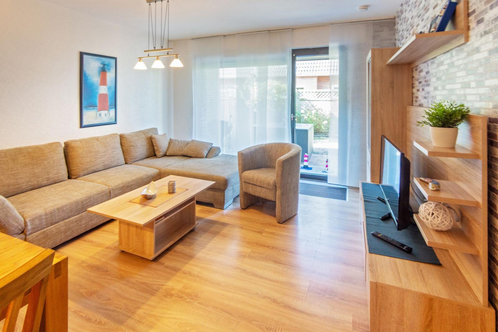 Wohnzimmer mit Sofa, Sessel, Couchtisch und Fernseher. Holzfußboden und Glasfront.