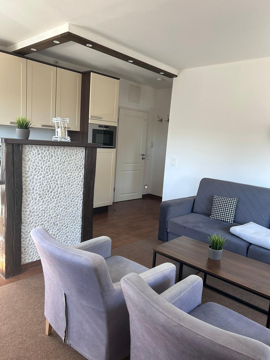 Wohnbereich mit Sofa, zwei Sesseln und Küchenbereich mit Steinwand.
